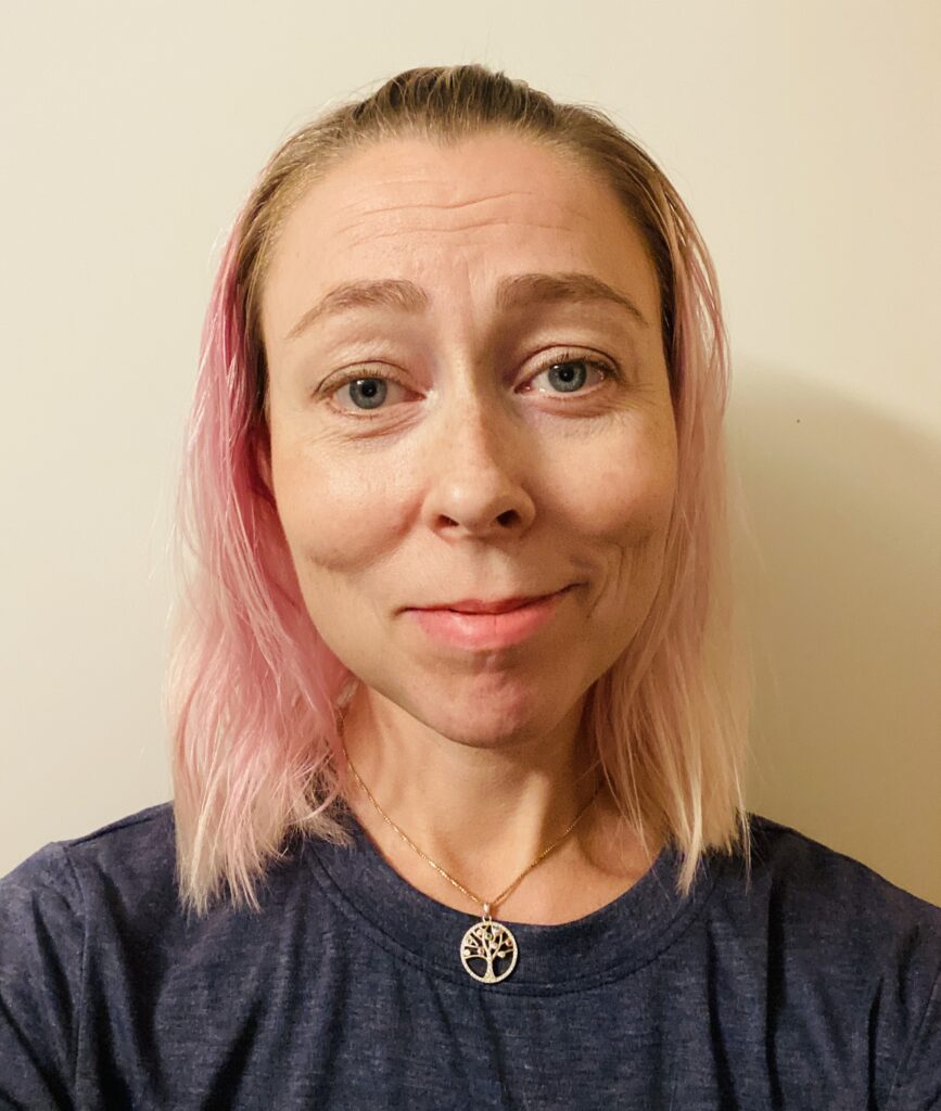 Profilbilde av kvinne med rosa-blondt hår og mørkeblå t-skjorte. Kvinnen smiller med munnen lukket og hun ser rett inn i kamera.